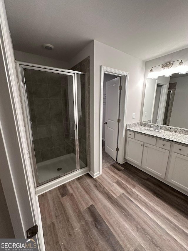 bathroom with a stall shower, vanity, baseboards, and wood finished floors