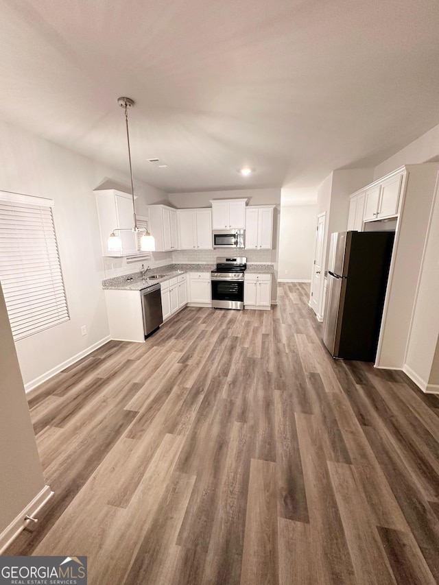 kitchen with white cabinets, appliances with stainless steel finishes, wood finished floors, light stone countertops, and pendant lighting