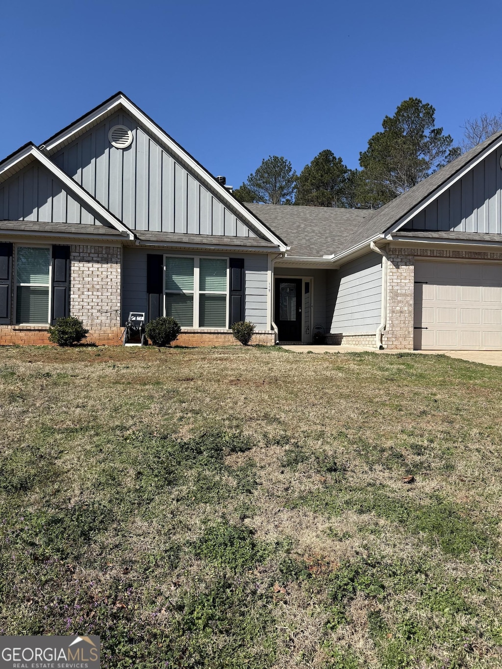 ranch-style home with an attached garage, a front yard, board and batten siding, and brick siding