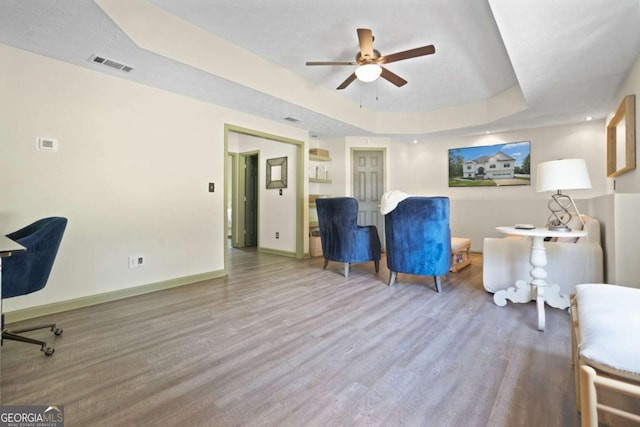 living area with baseboards, visible vents, a tray ceiling, and wood finished floors