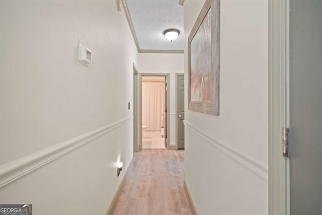 hall featuring light wood-type flooring, ornamental molding, and a textured ceiling