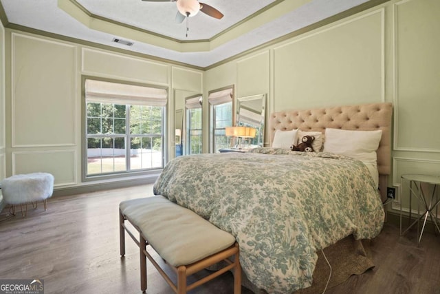 bedroom featuring a tray ceiling, ornamental molding, visible vents, and a decorative wall