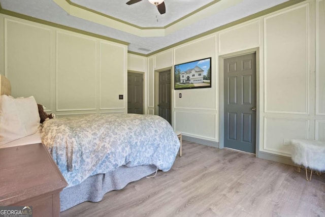 bedroom featuring ornamental molding, a tray ceiling, light wood-style floors, and a decorative wall