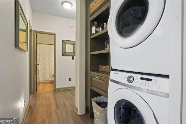 laundry area with stacked washer / dryer, laundry area, dark wood finished floors, and baseboards