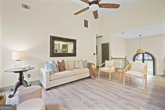 living area featuring light wood-style flooring, a high ceiling, visible vents, and a ceiling fan