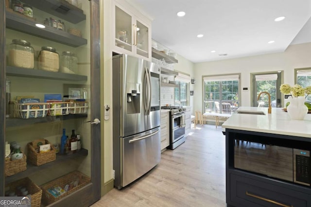 kitchen with light wood-style flooring, a sink, light countertops, appliances with stainless steel finishes, and glass insert cabinets