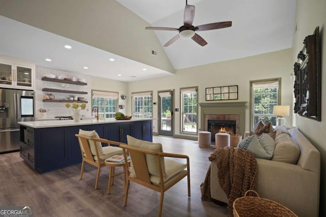 living area featuring ceiling fan, high vaulted ceiling, recessed lighting, a lit fireplace, and light wood-type flooring