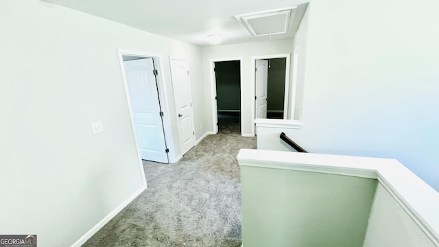 hallway featuring light carpet, attic access, baseboards, and an upstairs landing