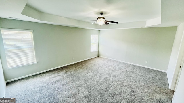 carpeted spare room with ceiling fan, a tray ceiling, visible vents, and baseboards