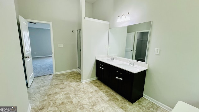 bathroom featuring double vanity, a high ceiling, a stall shower, a sink, and baseboards