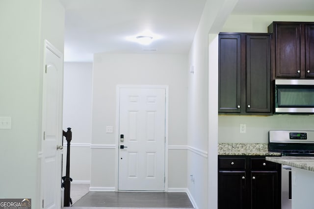 kitchen with light stone counters, appliances with stainless steel finishes, dark brown cabinetry, and baseboards