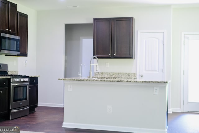 kitchen with dark brown cabinetry, light stone counters, stainless steel appliances, and dark wood-style flooring