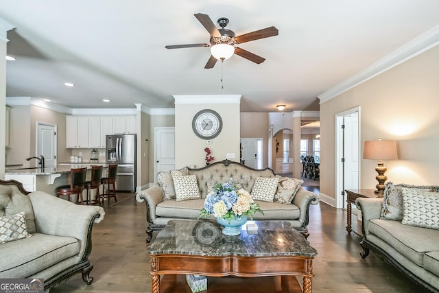 living area featuring arched walkways, ceiling fan, ornamental molding, and dark wood-style flooring