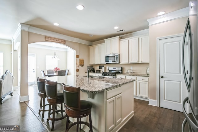 kitchen featuring arched walkways, a kitchen island with sink, white cabinetry, hanging light fixtures, and appliances with stainless steel finishes