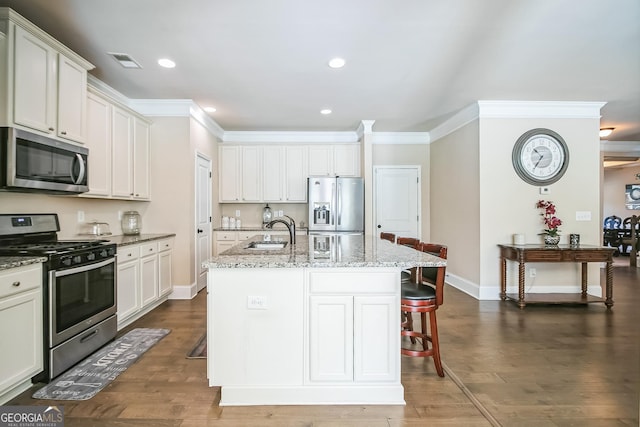 kitchen featuring a sink, visible vents, appliances with stainless steel finishes, light stone countertops, and an island with sink