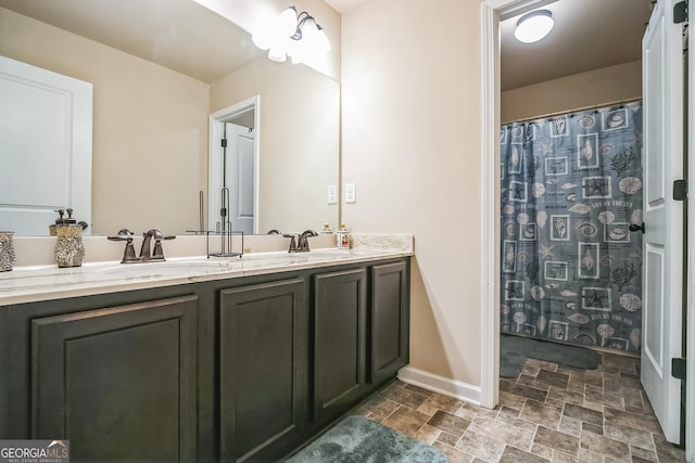 full bathroom with stone finish flooring, a sink, baseboards, and double vanity