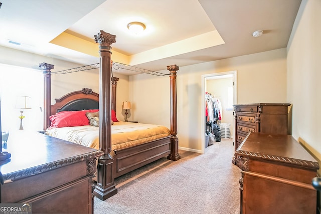 bedroom featuring light colored carpet, baseboards, a walk in closet, a raised ceiling, and decorative columns