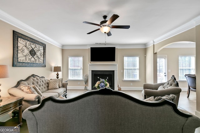 living area featuring arched walkways, ornamental molding, a fireplace, and a wealth of natural light