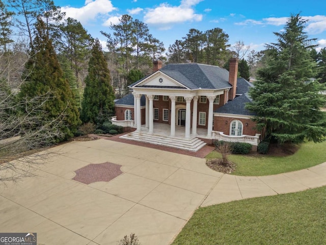 neoclassical / greek revival house with driveway, a chimney, a porch, roof with shingles, and a front lawn