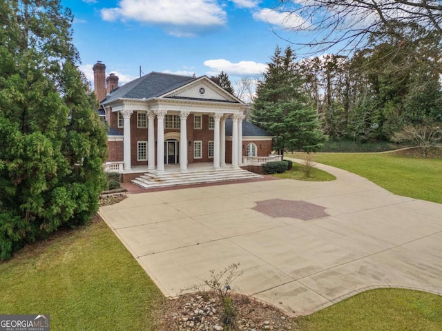 greek revival house with covered porch, brick siding, a chimney, and a front yard