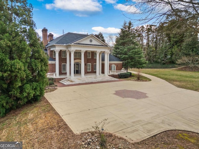 view of front of home with a front yard, covered porch, brick siding, and a chimney