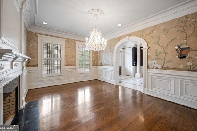 unfurnished dining area featuring wallpapered walls, a premium fireplace, arched walkways, and wainscoting