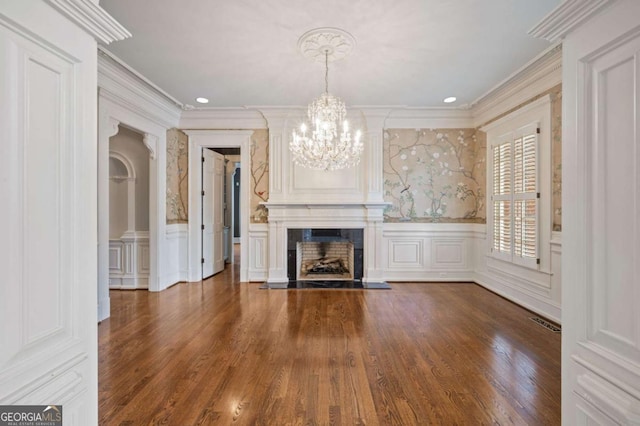 unfurnished living room with a notable chandelier, a decorative wall, a premium fireplace, visible vents, and ornamental molding