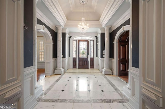 foyer entrance with decorative columns, wainscoting, ornamental molding, a tray ceiling, and a chandelier