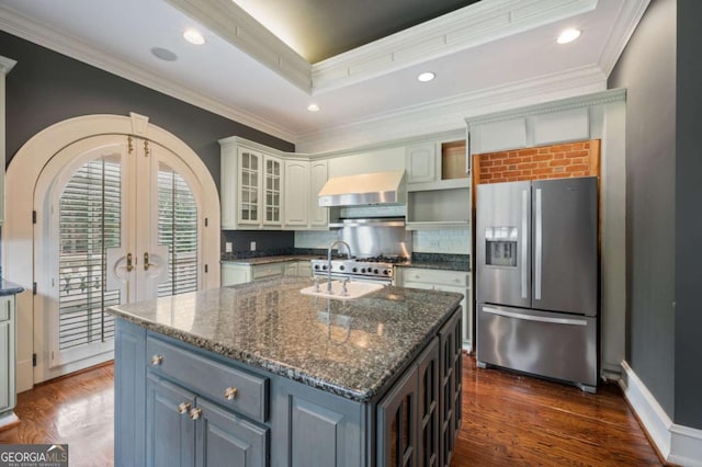 kitchen featuring french doors, a center island with sink, appliances with stainless steel finishes, white cabinets, and wall chimney range hood