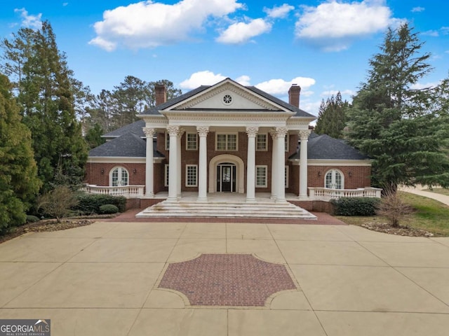 view of front of home with driveway, a chimney, and brick siding