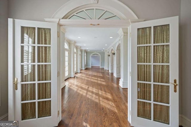 hallway with ornate columns, ornamental molding, wood finished floors, and recessed lighting