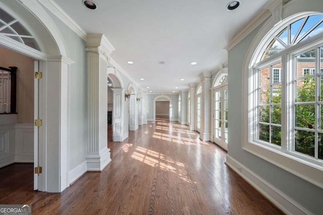 corridor featuring arched walkways, ornamental molding, dark wood-style flooring, and decorative columns