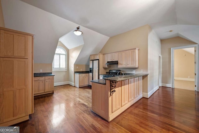 kitchen with a breakfast bar area, under cabinet range hood, a peninsula, refrigerator with ice dispenser, and dark stone counters