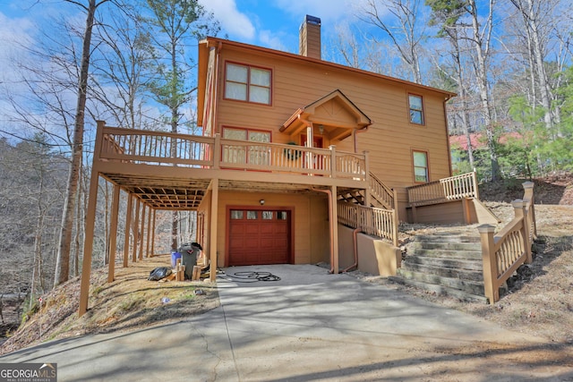 rustic home featuring a chimney, concrete driveway, an attached garage, a deck, and stairs