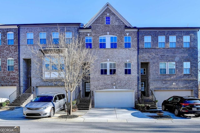 view of property featuring a garage, concrete driveway, brick siding, and stairway