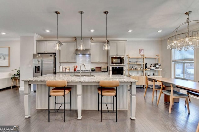 kitchen featuring pendant lighting, a center island with sink, appliances with stainless steel finishes, light stone countertops, and a kitchen bar