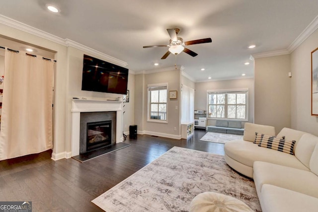 living room with a ceiling fan, baseboards, ornamental molding, dark wood-style floors, and a glass covered fireplace