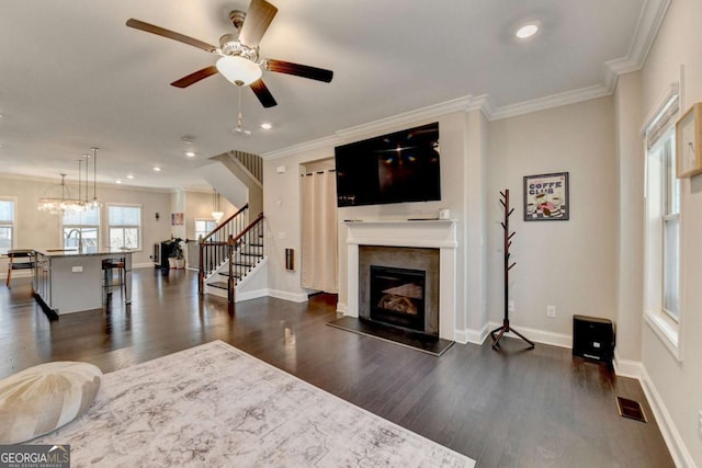 living room with stairway, dark wood-style flooring, visible vents, and crown molding