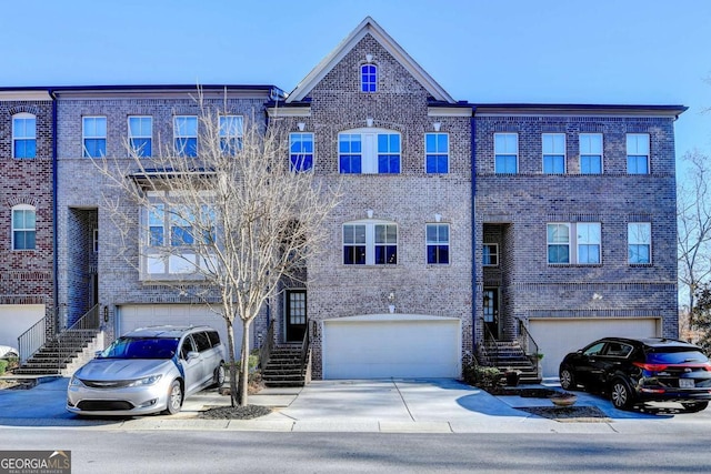 view of property featuring a garage, concrete driveway, brick siding, and stairway