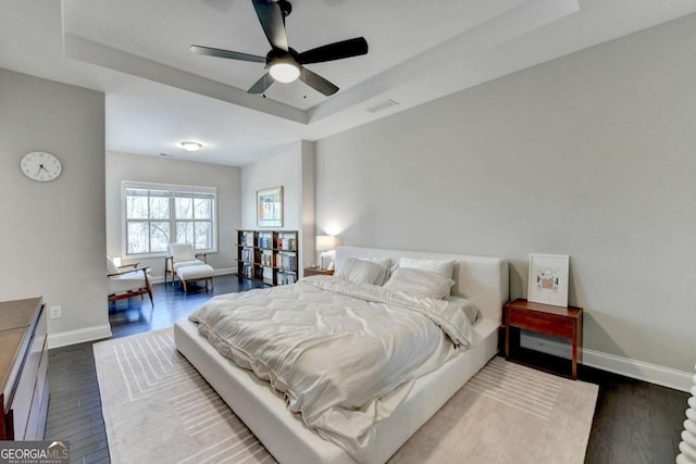 bedroom featuring a tray ceiling, dark wood finished floors, and baseboards