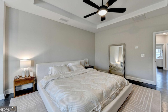 bedroom with a tray ceiling, dark wood-style flooring, visible vents, and baseboards