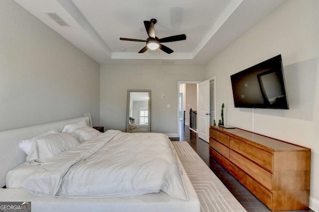 bedroom featuring dark wood-style flooring, a raised ceiling, visible vents, ceiling fan, and baseboards