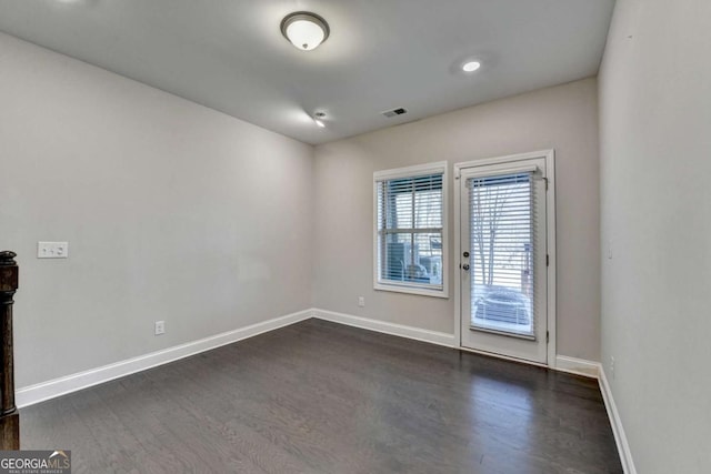 empty room featuring visible vents, baseboards, and dark wood-type flooring