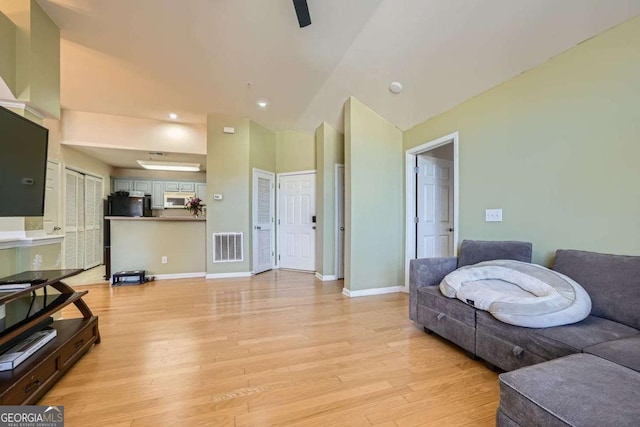 living area with lofted ceiling, baseboards, visible vents, and light wood finished floors