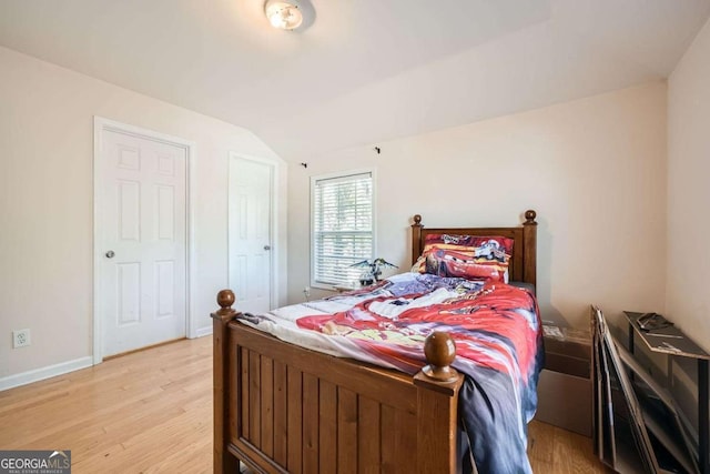 bedroom with baseboards, vaulted ceiling, and light wood-style floors