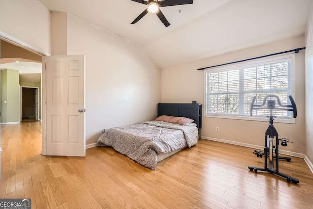 bedroom with arched walkways, baseboards, a ceiling fan, light wood-style flooring, and vaulted ceiling