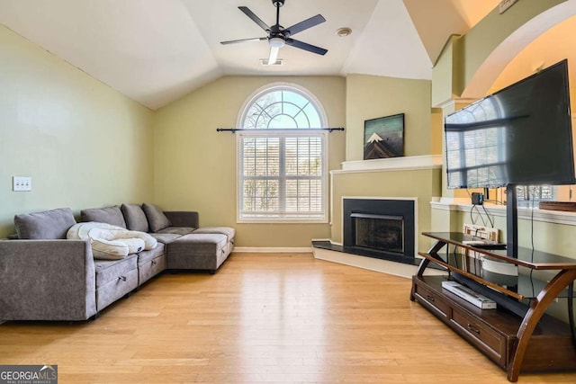 living area with a fireplace with raised hearth, ceiling fan, lofted ceiling, baseboards, and light wood finished floors