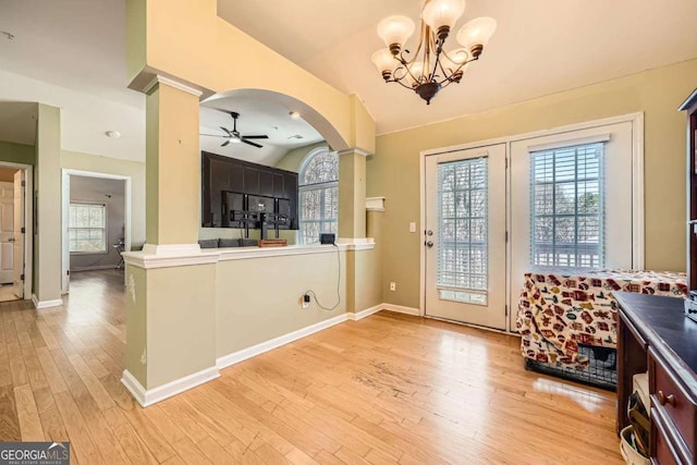 doorway featuring light wood finished floors, decorative columns, arched walkways, and ceiling fan with notable chandelier