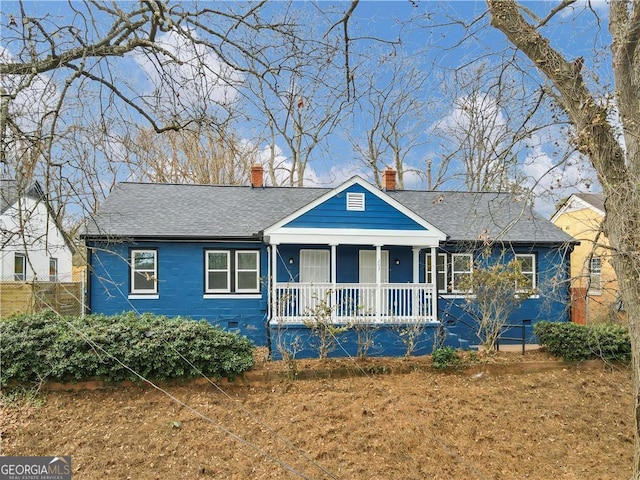 view of front of home with crawl space, a shingled roof, a chimney, and a porch