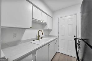 kitchen with wood finished floors, freestanding refrigerator, light countertops, white cabinetry, and a sink